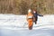 The little boy in overalls running through the snow toward the mother. Winter day in the coniferous forest. Back view