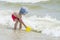 Little boy picking up sea water into a bucket for the game against the backdrop of the waves,