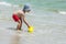 Little boy picking up sea water into a yellow bucket for the game against the backdrop of the waves.