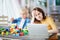 Little boy playing with construction blocks while his mother working on computer