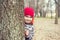 Little boy is playing hide and seek outdoors. Portrait of a cute little boy peeking from behind tree