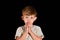 A little boy prays to God with his hands tucked open with his eyes open.