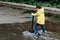 Little boy in raincoat and rubber boots playing in puddle. Fun on street.