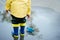 Little boy in raincoat and rubber boots playing in puddle. Happy little kid with paper ship