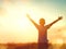 Little boy raising hands over sunset sky