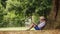 Little boy reading a book sitting at the foot of a big linden tree