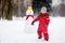 Little boy in red winter clothes having fun with snowman