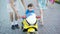 Little boy is riding on bright toy motorcycle in a city alley in summer day accompanied by his parents