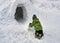 A little boy rolls a snow brick for an igloo, a traditional shelter of the northern peoples from the cold, made of snow