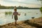 A little boy runs with a paper airplane along the river bank in