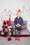 little boy in santa hat near christmas gnome toy, holding dwarf toy in hand in grey room. christmas decor and toys. kids