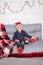 little boy in santa hat near christmas gnome toy, holding dwarf toy in hand in grey room. christmas decor and toys. kids