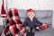 little boy in santa hat near christmas gnome toy, holding dwarf toy in hand in grey room. christmas decor and toys. kids