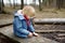 Little boy saws a branch with a small penknife on a large felled log while walking in the forest at spring