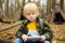 Little boy scout is orienteering in forest. Child is sitting and making notes in a notepad on background of teepee hut. Concepts