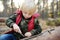 Little boy scout is playing with knife in the forest. Child cuts with a knife on a log