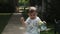 A little boy in shorts and sandals walks along a path among the grass and drinks water from a plastic bottle