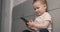 Little boy sits on the bed looking at the smartphone and smiling. The baby's holding a black cell phone. Slow motion