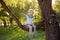 Little boy sits on a branch of a big tree and points with his finger. Child`s games. Active family time on nature. Hiking with