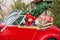 A little boy sits in a convertible santa`s car in a red hat with a Christmas tree