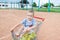 Little boy sits in a shopping trolley with tennis balls on clay court.