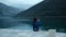 Little boy sits on shore and throws stones into water outdoors.