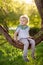 Little boy is sitting on a branch of tree and is dreaming. Child`s games. Active family time on nature. Hiking with little kids