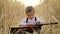 Little boy sitting in a golden wheat field and playing the guitar.