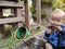 Little boy sitting on the ground looking at and picking his muddy hand