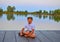 Little boy sitting on pier. Elementary age boy sitting on a wooden pier. Summer and childhood concept. Child on bench at the lake.