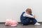 A little boy of six is offended and sits on the floor against a white wall next to a soft toy with his hands closed