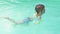 Little boy in sleeves and cap is swimming in the pool on vacation. boy swims in the pool in the tropics