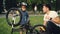 Little boy is spinning bicycle wheel and pedals while his father is talking to him on lawn in park on summer day. Family