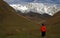 Little boy standing in front of snowy mountaines and autumn valley. Small traveller in wild nature, view from behind