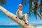 Little boy in a straw hat having fun on a coconut tree on a sandy tropical beach. The concept of travel and family holidays