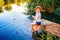 Little boy in straw hat sitting on the edge of a wooden dock and fishing in lake at sunset