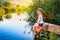 Little boy in straw hat sitting on the edge of a wooden dock and fishing in lake at sunset