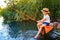 Little boy in straw hat sitting on the edge of a wooden dock and fishing in lake at sunset