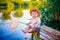 Little boy in straw hat sitting on the edge of a wooden dock and fishing in lake at sunset