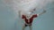 A little boy swims underwater in the water jets in the pool in a Santa Claus suit with his arms outstretched