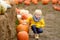 Little boy on a tour of a pumpkin farm at autumn. Child sitting near giant pumpkin