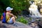 Little boy traveler with backpack sits near falls