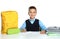 Little boy in uniform doing assignment at desk against white background