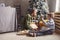 Little boy unpacking Christmas gift with mother while sitting together by beautiful decorated fake xmas tree