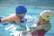 Little boy using the kickboard for learning to swim with trainer in the swimming pool