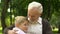 Little boy walking to grandfather sitting on bench and hugging him with love