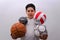 A little boy wearing a white sports shirt holding soccer, football, basketball and volleyball balls