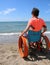 Little boy in a wheelchair looks at the sea from the beach