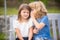 Little boy whispers to lovely girl in ear. Brother and sister playing in spring park outdoors. Little boy and girl kids