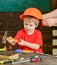 Little boy working with hammer. Daddy taking care of sons safety. Male hands holding orange protective helmet. Small kid